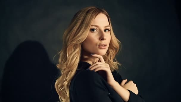 Blondine mit lockigem Haar posiert auf schwarzem Hintergrund im Studio — Stockvideo