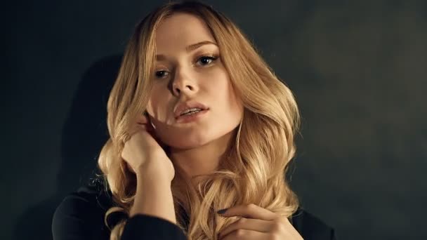 Blonde vrouw met gouden krulhaar poseren op een zwarte achtergrond in de studio — Stockvideo