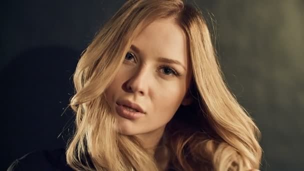 Блондинка с кудрявыми золотыми волосами позирует на черном фоне в студии — стоковое видео