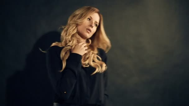 Блондинка з кучерявим волоссям позує на чорному тлі в студії — стокове відео