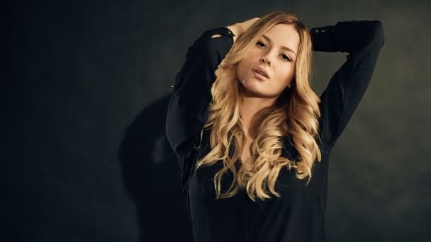 Blondine mit lockigem Haar posiert auf schwarzem Hintergrund im Studio — Stockvideo