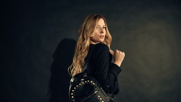 Femme blonde aux cheveux bouclés en vêtements sombres posant sur fond noir en studio — Video