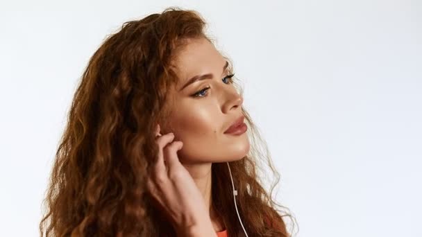 Brunette woman model with curly hair listening music on white background in studio — Stock Video