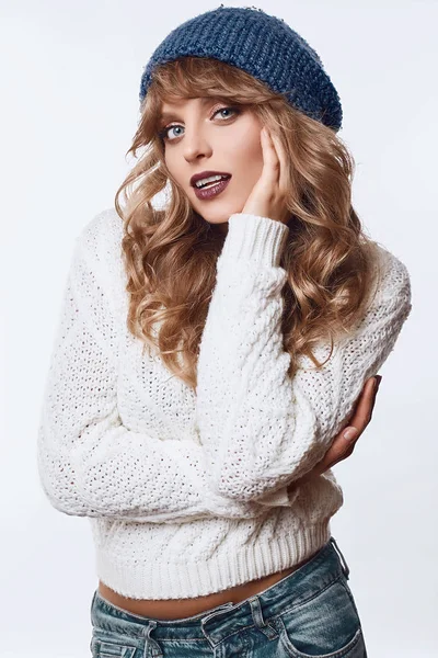 Положительная блондинка в свитере и шляпе на белом фоне — стоковое фото