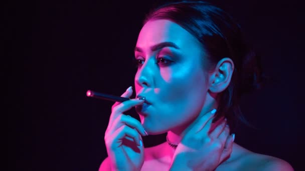 ネオン色のスタジオの光で電子タバコを吸ってするグラマー魅惑的なゴージャスなブルネットの女性の肖像画 — ストック動画