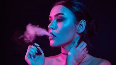 Ağır çekim portre glamour baştan çıkarıcı muhteşem bir esmer kadın sigara elektronik sigara neon renkli stüdyo ışık