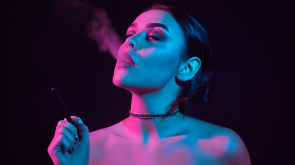 ネオン色のスタジオの光の魅力魅惑的なゴージャスなブルネット女性喫煙電子タバコのスローモーションの肖像画 — ストック動画