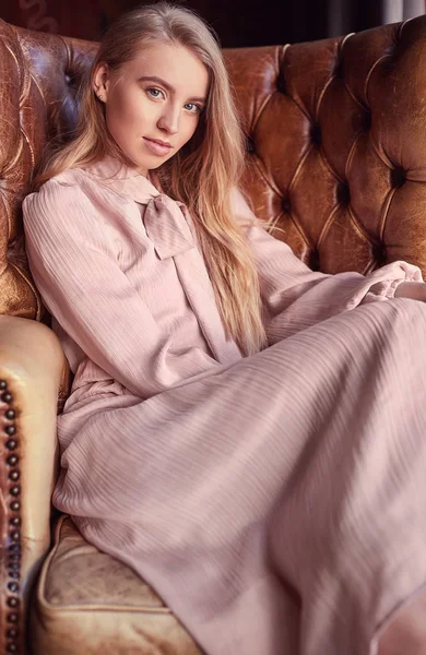 Vacker elegant blond kvinna i rosa klänning sitter i läderfåtölj — Stockfoto