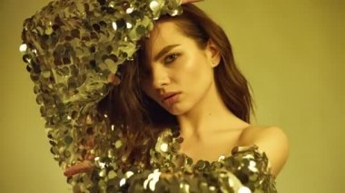 Parlak bir moda şehvetli güzel bir esmer kadın portresi elbise pul Studio'da parlak altın arka plan üzerinde poz
