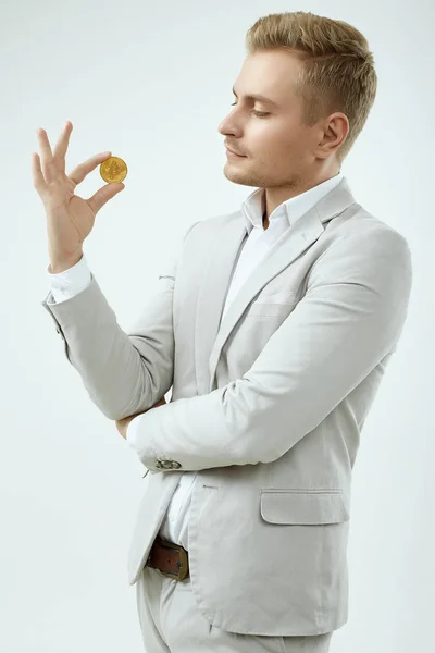 穿着时尚灰色西装的漂亮金发男模拿着一枚比特币 — 图库照片