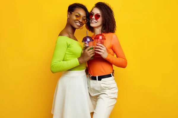 Két fiatal, gyönyörű hipszter lány színes nyári ruhában koktélokkal. — Stock Fotó