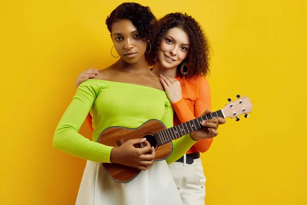 Duas jovens meninas hipster bonitas em roupas coloridas de verão com guitarra pequena — Fotografia de Stock