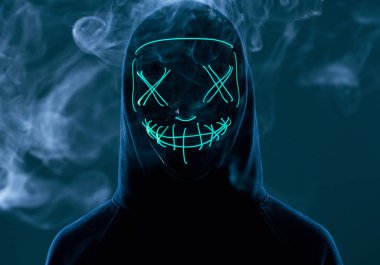 İsimsiz bir adam renkli bir dumanın içinde yüzünü neon maskenin arkasına gizliyor.