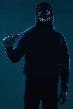 Siyah kapüşonlu ve neon maskeli beysbol sopalı isimsiz bir suçlu.