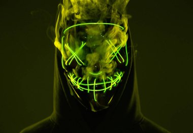 İsimsiz bir adam renkli bir dumanın içinde yüzünü neon maskenin arkasına gizliyor.