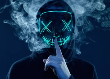 İsimsiz bir adam renkli bir dumanın içinde yüzünü neon maskenin arkasına gizliyor.