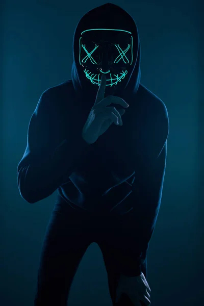 Anonymer Mann in schwarzem Kapuzenpulli versteckt sein Gesicht hinter einer Neonmaske — Stockfoto