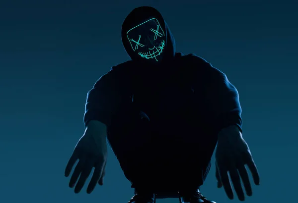 Siyah kapüşonlu isimsiz bir adam yüzünü neon bir maskenin arkasına gizliyor. — Stok fotoğraf
