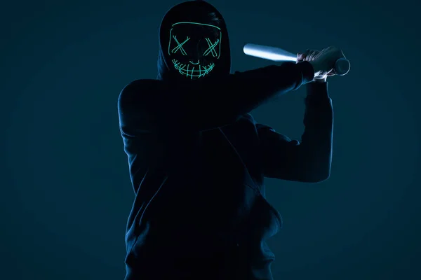 Hombre criminal anónimo con bate de béisbol con capucha negra y máscara de neón — Foto de Stock