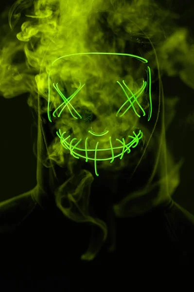 İsimsiz bir adam renkli bir dumanın içinde yüzünü neon maskenin arkasına gizliyor. — Stok fotoğraf