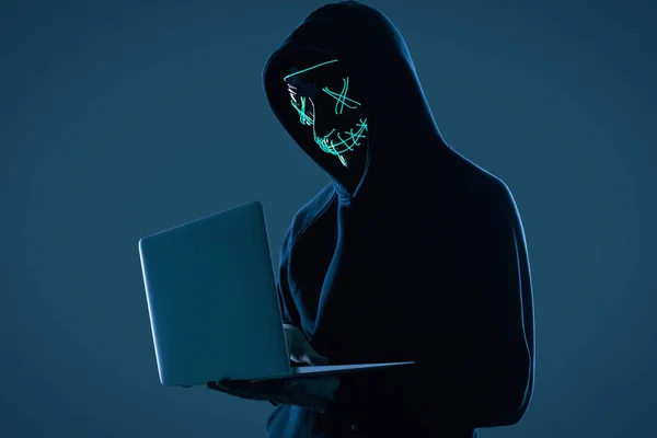 Anonym man i svart luvtröja och neonmask hacka sig in i en dator — Stockfoto