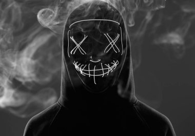 Kimliği belirsiz bir adam renkli bir dumanın içinde yüzünü neon maskenin arkasına gizliyor.