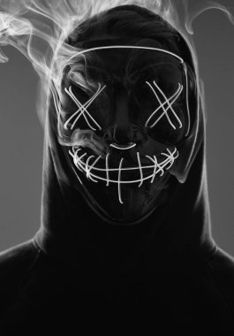 Kimliği belirsiz bir adam renkli bir dumanın içinde yüzünü neon maskenin arkasına gizliyor.