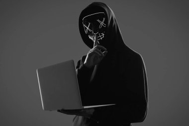 Anonymous man in a black hoodie and neon mask hacking into a com clipart