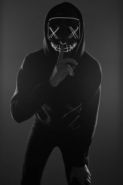 Anonymous man in black hoodie hiding his face behind a neon mask