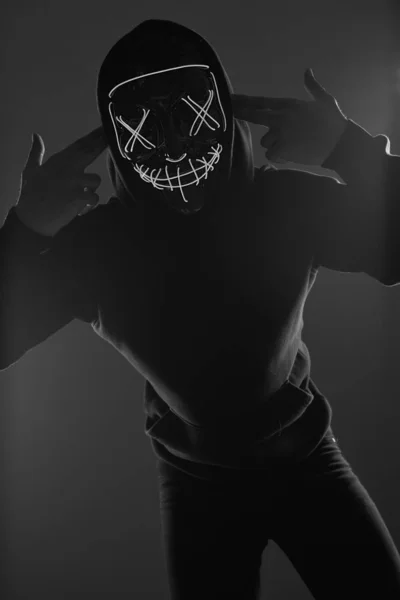 Anonymní muž v černé mikině skrývá tvář za neonovou maskou — Stock fotografie
