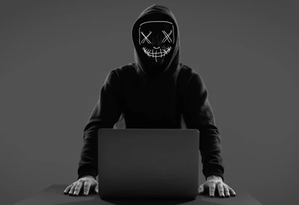 Hombre anónimo con capucha negra y máscara de neón hackeando una comunicación — Foto de Stock