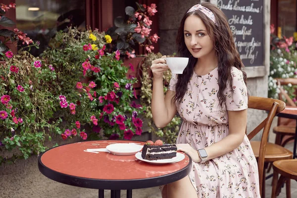 Jeune belle fille lumineuse dans une robe d'été assis à une table de café européenne — Photo