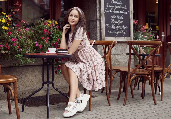 Jeune belle fille lumineuse dans une robe d'été assis à une table de café européenne — Photo