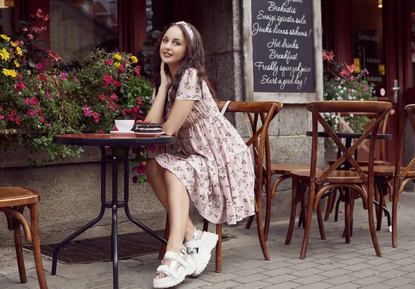 Jeune belle fille lumineuse dans une robe d'été assis à une table de café européenne — Photo