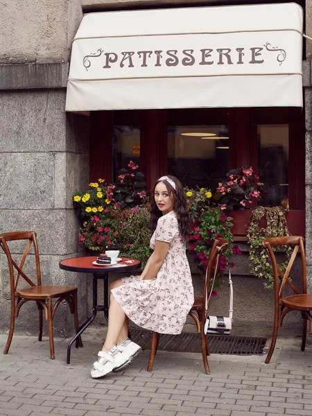 Jeune belle fille lumineuse dans une robe d'été assis à une table de café européenne — Photo