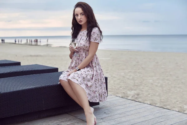 Joven hermosa chica brillante en un vestido de verano sentado en la playa —  Fotos de Stock