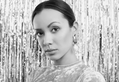 Göz kamaştırıcı, zarif, esmer Latin kadının portresi. Pembe elbiseli, parlak arkaplanda poz veriyor.