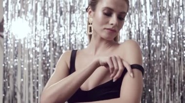 Stüdyodaki parlak süslemelerle izole edilmiş siyah elbise giyen zarif, zarif sarışın kadının portresi.