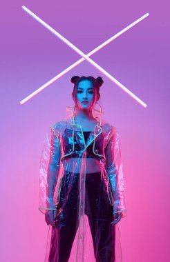 Renkli parlak neon ışıkların etrafında şık bir yağmurlukla stüdyoda poz veren zarif Asyalı bir kadının portresi.