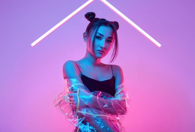 Renkli parlak neon ışıkların etrafında şık bir yağmurlukla stüdyoda poz veren zarif Asyalı bir kadının portresi.