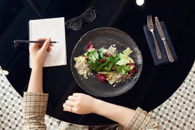 Sağlıklı gıda ve diyet planlama konsepti. Defter kullanan ve taze salata yiyen bir kadın.