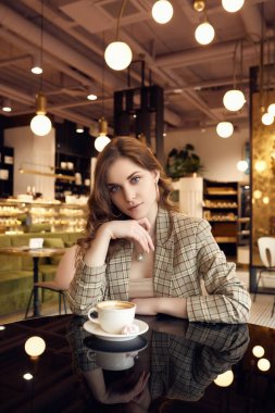 Kendine güvenen genç bir iş kadınının portresi. Sıradan giyinmiş, kafenin içinde kahve içiyor.