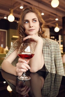 Restoranın içinde bir bardak kırmızı şarapla zarif, esmer bir kadının portresi.