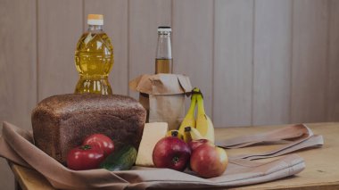 Ekmek, ayçiçeği yağı, domates, muz, salatalık, elma, elma, elma ve peynir dolu mutfak masasında..