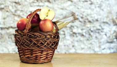 Kırmızı taze elma sepeti ve ahşap bir masada bir şişe elma şarabı..