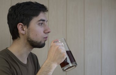 Genç, kısa saçlı, sakallı esmer bir adam cam bardaktan kvass içiyor..