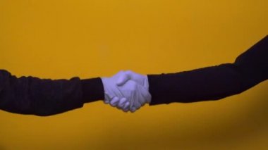 Koronavirüs salgını sırasında sarı arka planda mavi eldivenli iki kişinin el sıkışması..