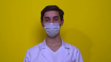 Beyaz önlüklü ve tıbbi maskeli doktor yorucu bir günün ardından yorgundu. Sarı arkaplanda Coronavirus kavramı.