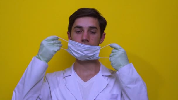 白いコートを着た医者が彼の顔に医療マスクをつけた 黄色の背景にコロナウイルスの概念 — ストック動画