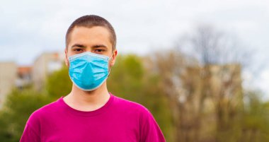 Arkaplanda pembe tişört ve mavi tıbbi maske takan yakışıklı, beyaz bir adam. Kopya alanı ile Coronavirus kavramı.